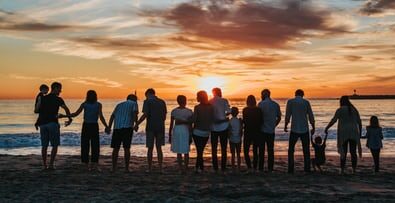 People holding hands looking out to the ocean during a sunset.